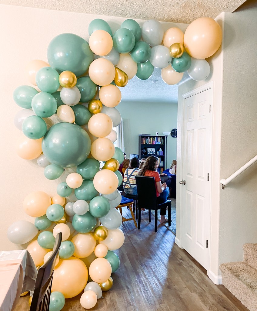 The entry to a room with a large balloon garland with gold, cream, and light and dark sage green balloons.