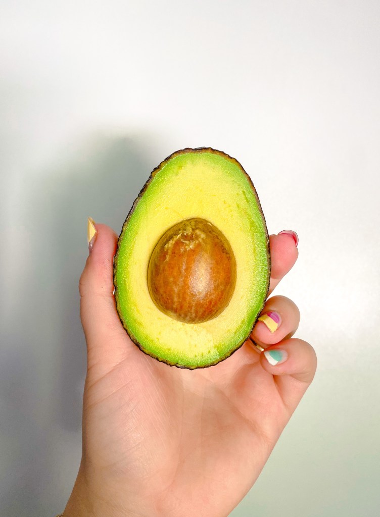 A hand holding half of a perfectly ripe green avocado.