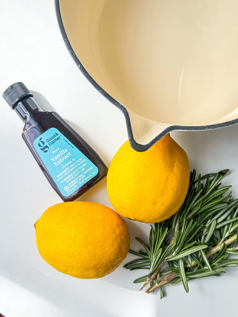 the ingredients needed for a Williams Sonoma simmer pot with a white background: a cast iron pot, lemons, vanilla extract, and rosemary,