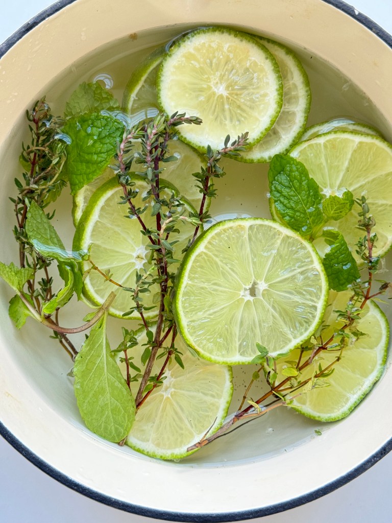 Ingredients needed to make a floral simmer pot: lime slices, thyme, and mint in a white enamel cast iron pot.