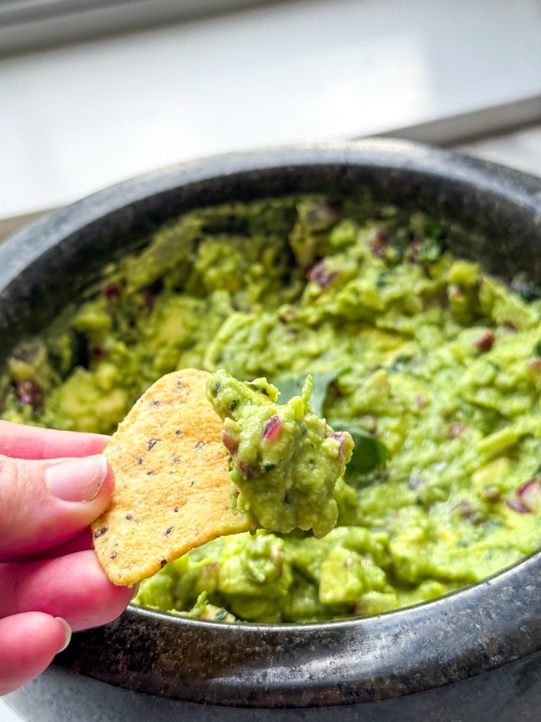 a corn chip being dipped in fresh guacamole made with a mortar and pestle