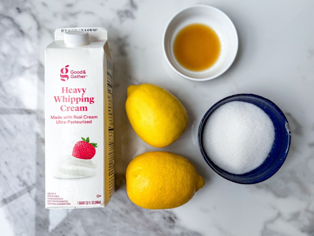 Lemon Posset in Lemon Shell ingredients on a marble backdrop: lemons, vanilla, cream, and sugar.