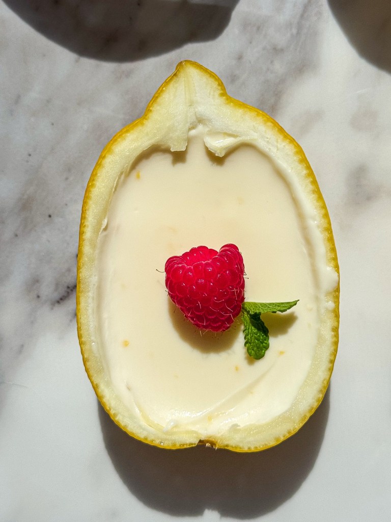Completed Lemon Posset in Lemon Shell, garnished with a juicy, plump raspberry and a small sprig of mint. 
