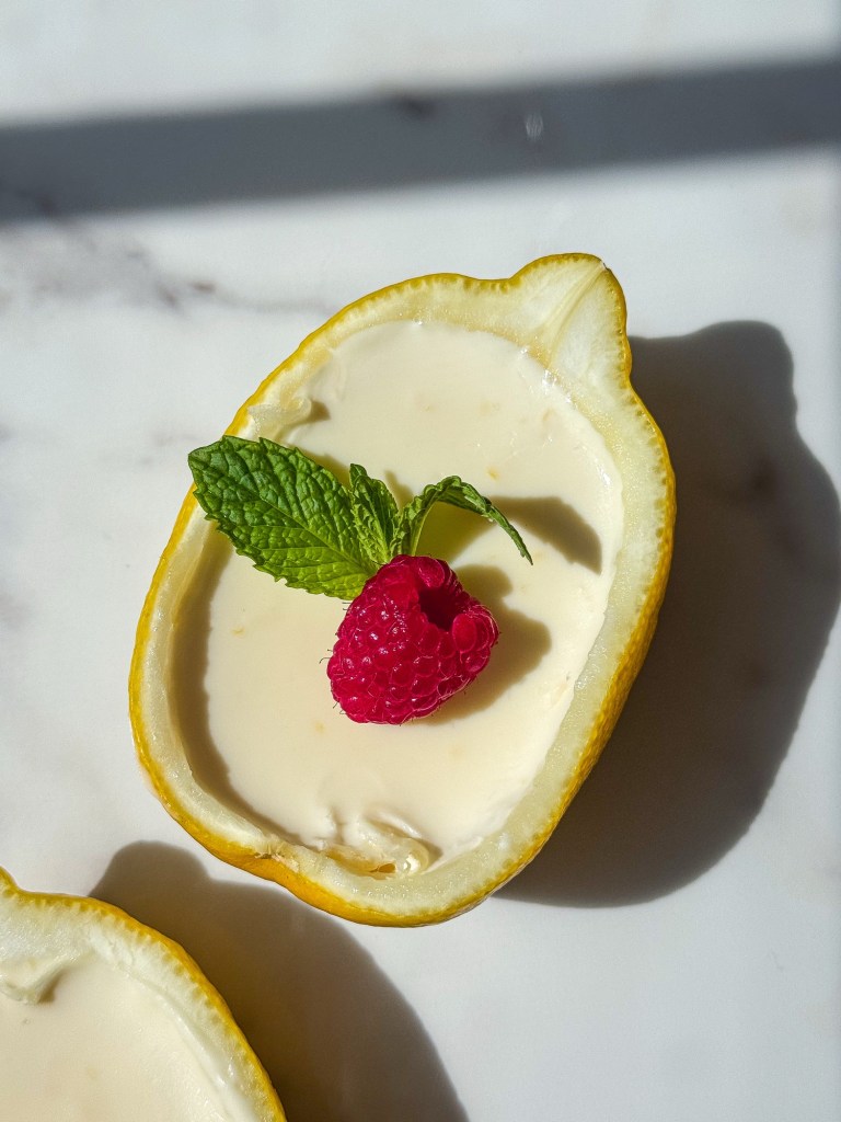Lemon Posset in Lemon Shell, garnished with a bright and vibrant raspberry and a small sprig of mint. 