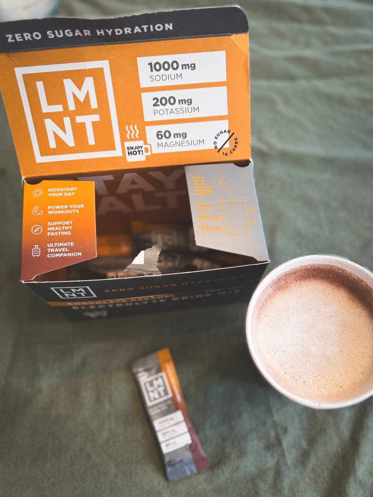 an open box of LMNT with a cup full of frothy and delicious low carb hot chocolate LMNT beside it