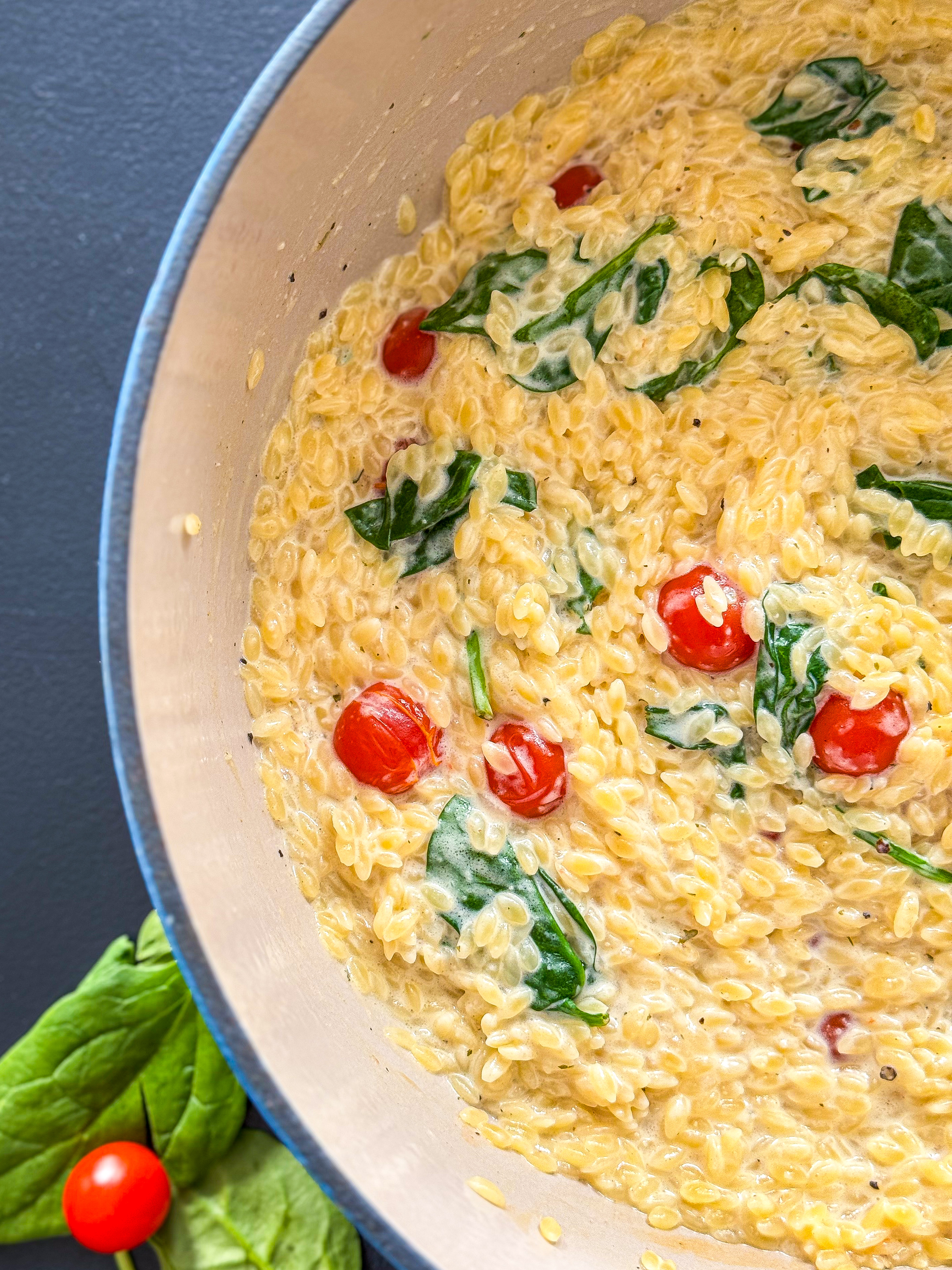 a large dutch oven pot full of creamy orzo, spinach, and cherry tomatoes, flavored with Boursin cheese